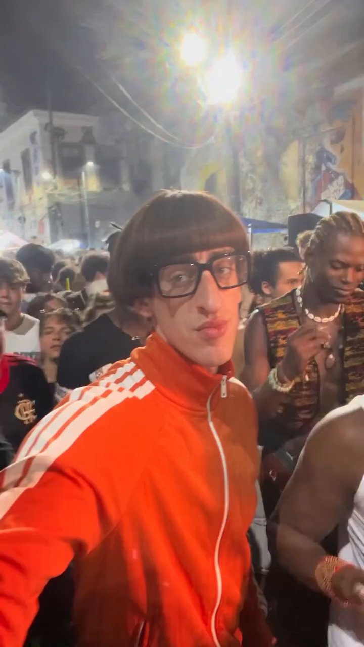 Quadro do vídeo-base, com uma pessoa de jaqueta laranja em primeiro plano